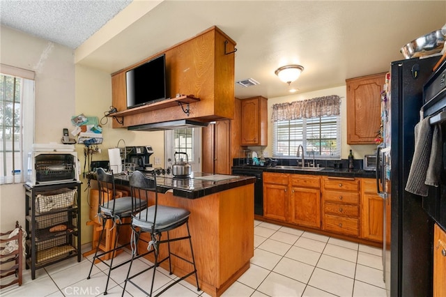 19722 Tajauta Ave, Carson, CA 90746 - kitchen featuring a peninsula, brown cabinets, black appliances, light tile patterned floors, and a textured ceiling