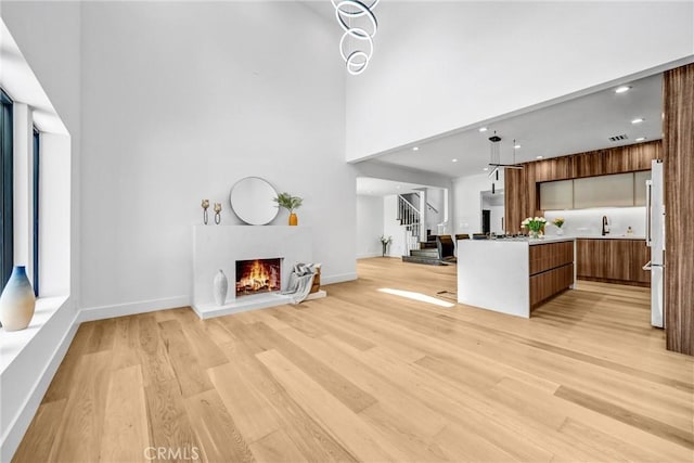 1027 N Lamer St, Burbank, CA 91506 - unfurnished living room with stairway, light wood-style flooring, a warm lit fireplace, recessed lighting, and a high ceiling