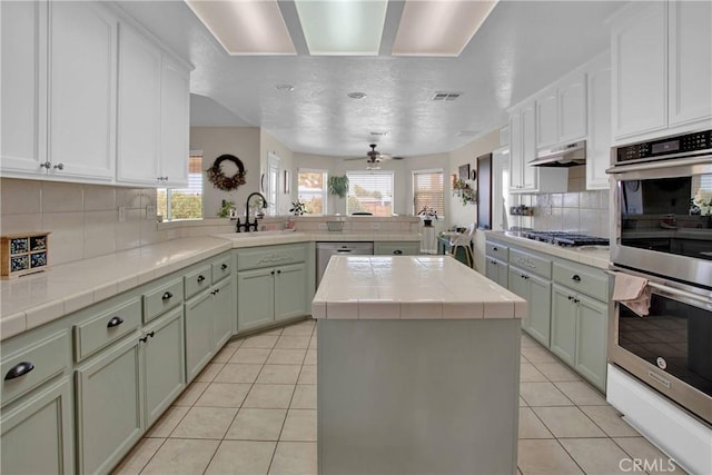 7330 Smoke Tree Rd, Phelan, CA 92371 - kitchen with appliances with stainless steel finishes, a peninsula, tasteful backsplash, light tile patterned floors, and a kitchen island