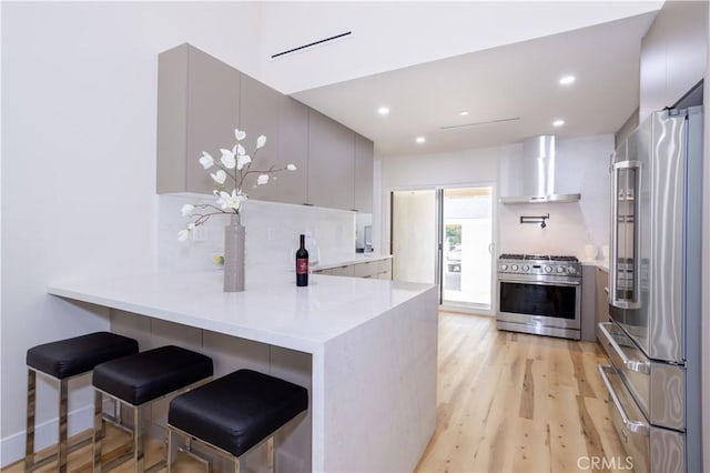 17905 Bullock St, Encino, CA 91316 - kitchen with high end appliances, wall chimney exhaust hood, a peninsula, light wood-style floors, and recessed lighting