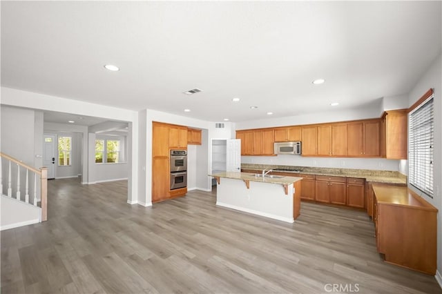 36845 Gemina Ave, Murrieta, CA 92563 - kitchen featuring stainless steel appliances, recessed lighting, a kitchen bar, an island with sink, and light wood-type flooring