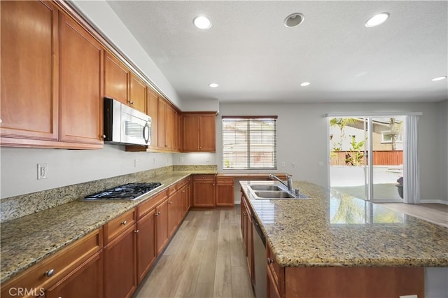 36845 Gemina Ave, Murrieta, CA 92563 - kitchen with stainless steel appliances, light wood finished floors, recessed lighting, brown cabinets, and a center island with sink