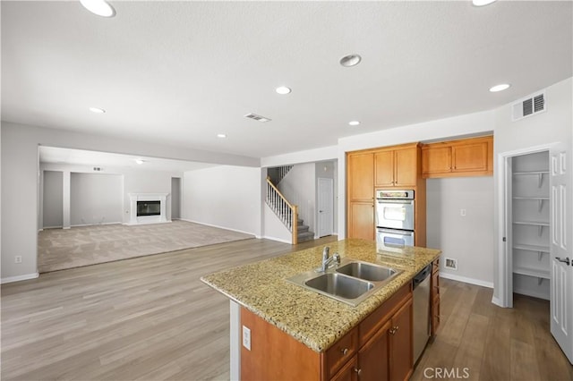 36845 Gemina Ave, Murrieta, CA 92563 - kitchen featuring stainless steel appliances, light wood-style floors, an island with sink, a glass covered fireplace, and recessed lighting