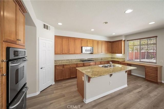 36845 Gemina Ave, Murrieta, CA 92563 - kitchen featuring appliances with stainless steel finishes, light wood-type flooring, light stone countertops, brown cabinetry, and recessed lighting