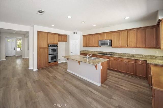 36845 Gemina Ave, Murrieta, CA 92563 - kitchen featuring appliances with stainless steel finishes, brown cabinetry, recessed lighting, light stone counters, and dark wood finished floors