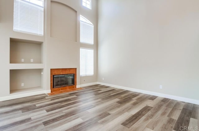 4620 Los Alamos Way Unit C, Oceanside, CA 92057 - unfurnished living room with built in features, a towering ceiling, wood finished floors, and a tiled fireplace