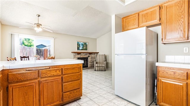 7339 Greenbriar Pl, Rancho Cucamonga, CA 91730 - kitchen with freestanding refrigerator, a ceiling fan, tile countertops, a textured ceiling, and a fireplace