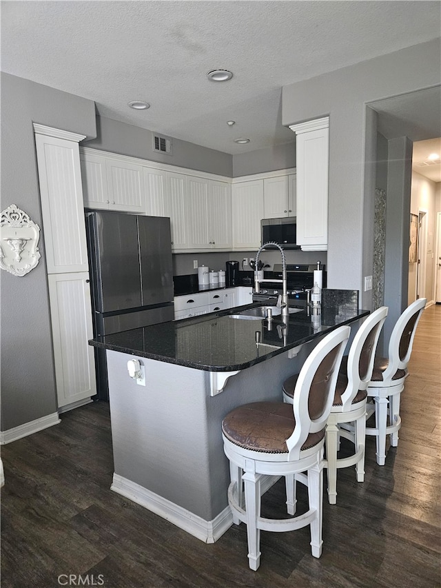 785 Harbor Cliff Way Unit 177, Oceanside, CA 92054 - kitchen featuring dark wood-style flooring, white cabinets, stainless steel microwave, a breakfast bar, and freestanding refrigerator