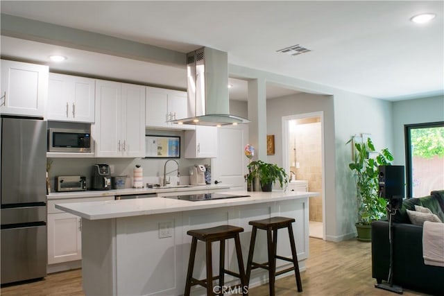 542 N Kilkea Dr, Los Angeles, CA 90048 - kitchen featuring appliances with stainless steel finishes, island exhaust hood, white cabinets, a kitchen breakfast bar, and recessed lighting