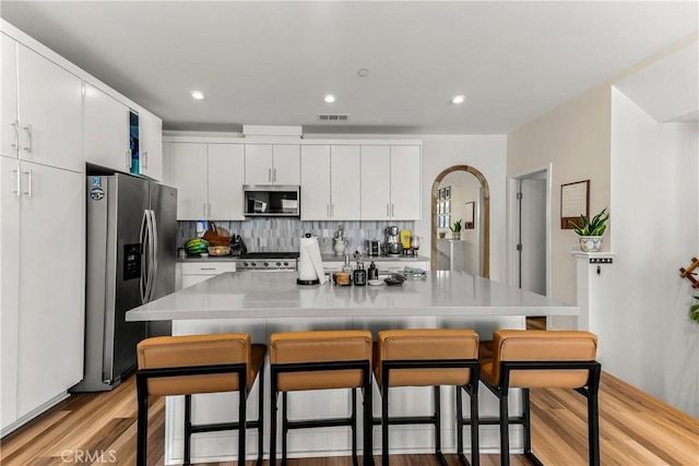 1206 W Cara Dr, Anaheim, CA 92805 - kitchen with appliances with stainless steel finishes, a kitchen bar, light wood-style flooring, white cabinetry, and backsplash