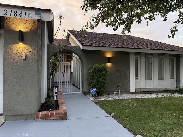 21841 Zuni Dr, Lake Forest, CA 92630 - view of exterior entry featuring stucco siding, a gate, a lawn, and roof with shingles