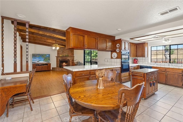 41050 Mesa Robles Cir, Temecula, CA 92592 - kitchen with brown cabinetry, light tile patterned flooring, ceiling fan, a fireplace, and tile countertops
