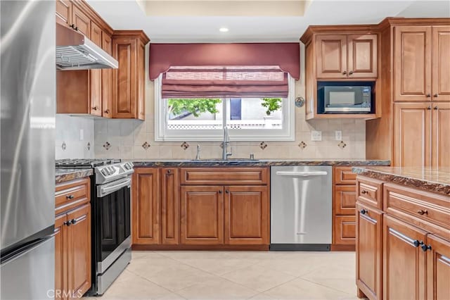 20002 Tomlee Ave, Torrance, CA 90503 - kitchen featuring appliances with stainless steel finishes, under cabinet range hood, brown cabinetry, dark stone counters, and a raised ceiling