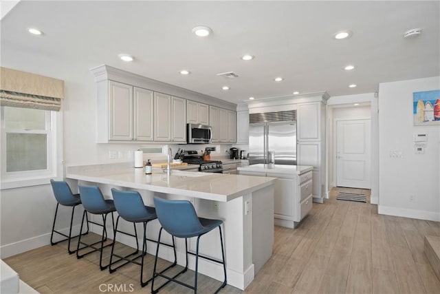 3312 W Oceanfront, Newport Beach, CA 92663 - kitchen with appliances with stainless steel finishes, a peninsula, a breakfast bar, light countertops, and light wood-style flooring