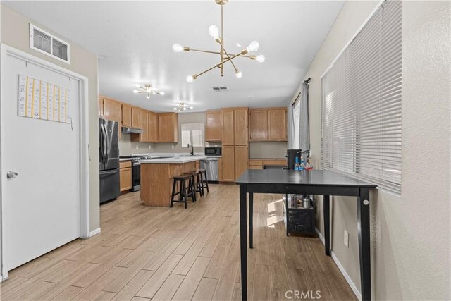 1142 Juniper Ct, San Jacinto, CA 92582 - kitchen featuring stainless steel appliances, under cabinet range hood, a chandelier, light wood-type flooring, and a breakfast bar area