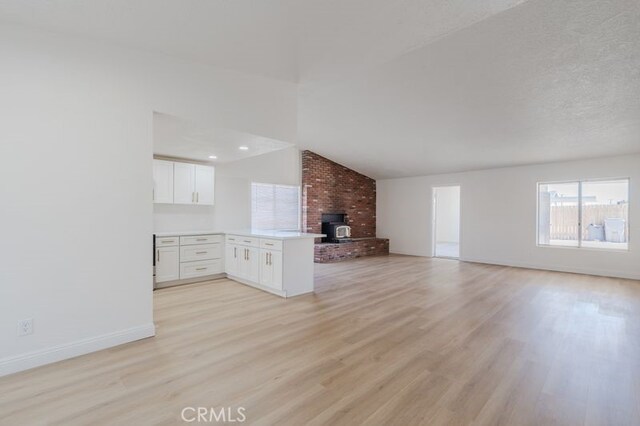 16233 Manzanita St, Hesperia, CA 92345 - unfurnished living room featuring light wood-style floors, vaulted ceiling, and a wood stove