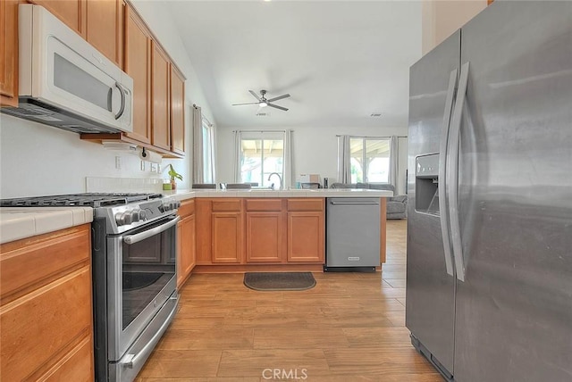 1503 Lynwood Way, Highland, CA 92346 - kitchen with appliances with stainless steel finishes, a peninsula, tile counters, open floor plan, and light wood-type flooring