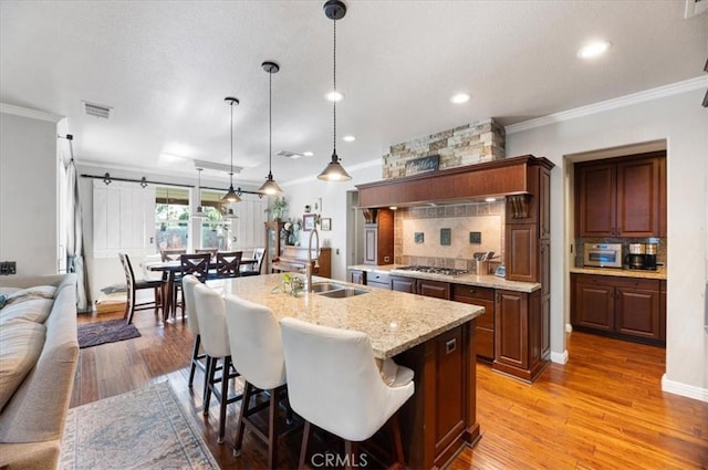 22517 Skipping Stone Dr, Saugus, CA 91350 - kitchen with crown molding, stainless steel gas stovetop, decorative backsplash, light wood-style floors, and an island with sink
