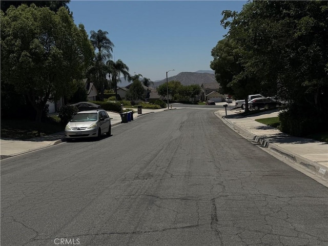 23020 Jensen Ct, Grand Terrace, CA 92313 - view of asphalt street with sidewalks, street lights, curbs, a mountain view, and a residential view