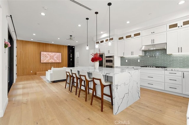10413 Saint Anna Pl, Fountain Valley, CA 92708 - kitchen with under cabinet range hood, backsplash, light wood-style flooring, a large island, and recessed lighting