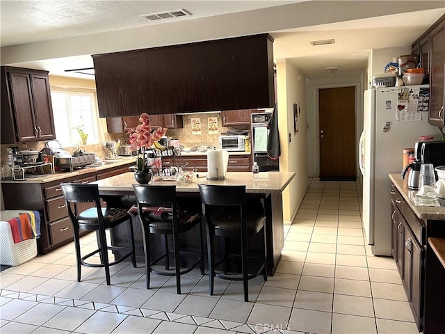 1061 N Perris Blvd, Perris, CA 92571 - kitchen featuring freestanding refrigerator, dark brown cabinetry, a breakfast bar, light tile patterned floors, and a kitchen island