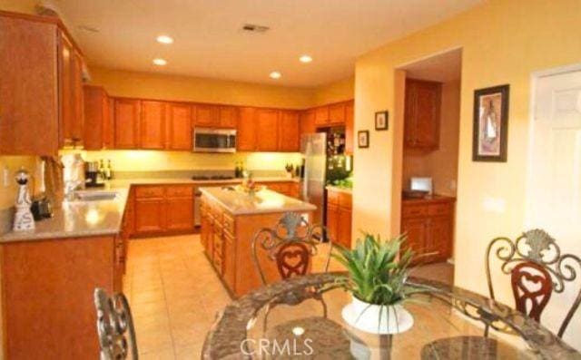 45211 Tioga St, Temecula, CA 92592 - kitchen with stainless steel microwave, light countertops, a center island with sink, light tile patterned floors, and freestanding refrigerator
