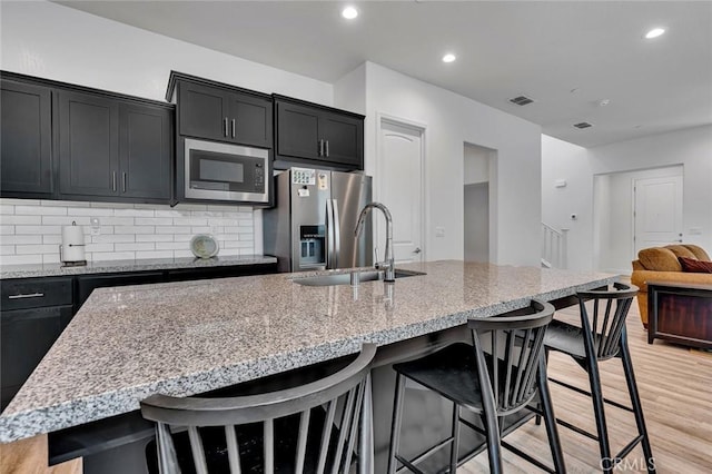 253 Peters Ln S, Madera, CA 93636 - kitchen featuring stainless steel appliances, dark cabinets, a kitchen breakfast bar, tasteful backsplash, and light stone counters