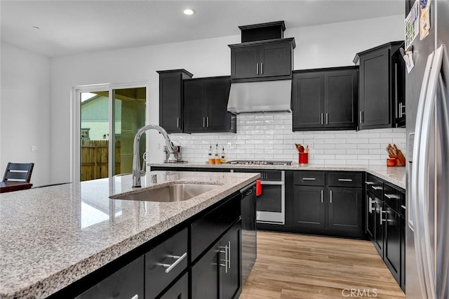 253 Peters Ln S, Madera, CA 93636 - kitchen featuring stainless steel appliances, dark cabinetry, ventilation hood, decorative backsplash, and light stone counters