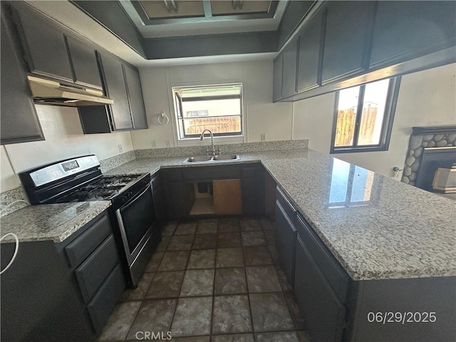 467 Stanford Dr, Barstow, CA 92311 - kitchen featuring stainless steel range with gas stovetop, a peninsula, under cabinet range hood, dark stone finish floors, and light stone countertops