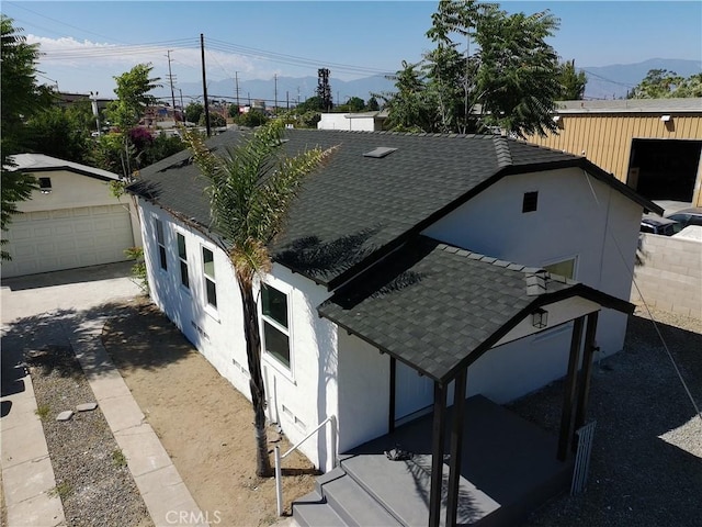 817 Orange Grove Ave, Colton, CA 92324 - view of side of home featuring a shingled roof, an outbuilding, stucco siding, a mountain view, and a garage