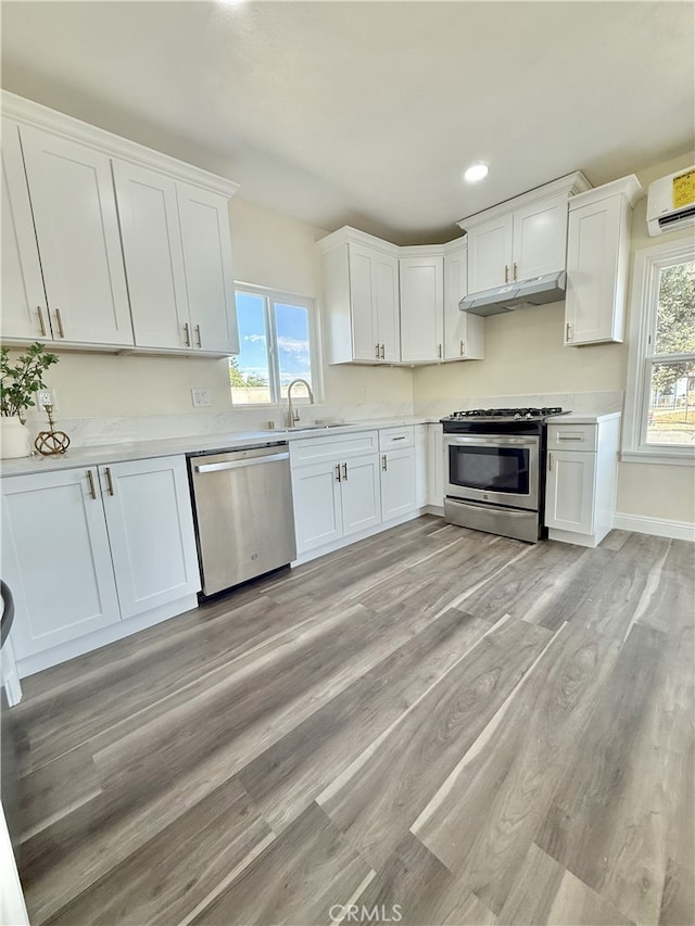 817 Orange Grove Ave, Colton, CA 92324 - kitchen with stainless steel appliances, white cabinetry, light countertops, a wall mounted air conditioner, and light wood finished floors