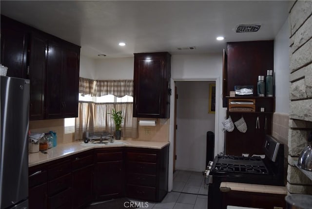 6718 Del Rosa Dr, San Bernardino, CA 92404 - kitchen with freestanding refrigerator, black gas range oven, light countertops, light tile patterned floors, and tasteful backsplash