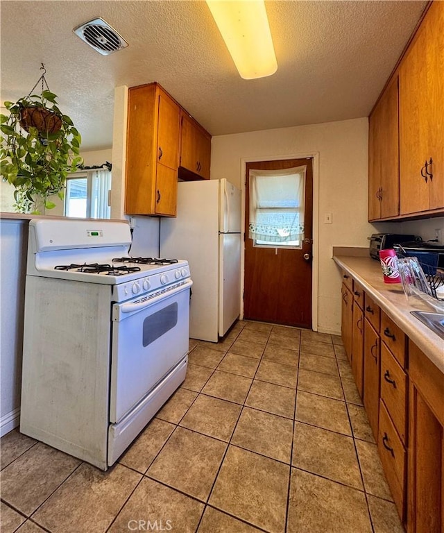 751 Yucca Ave, Barstow, CA 92311 - kitchen featuring white appliances, brown cabinetry, a textured ceiling, light countertops, and light tile patterned flooring