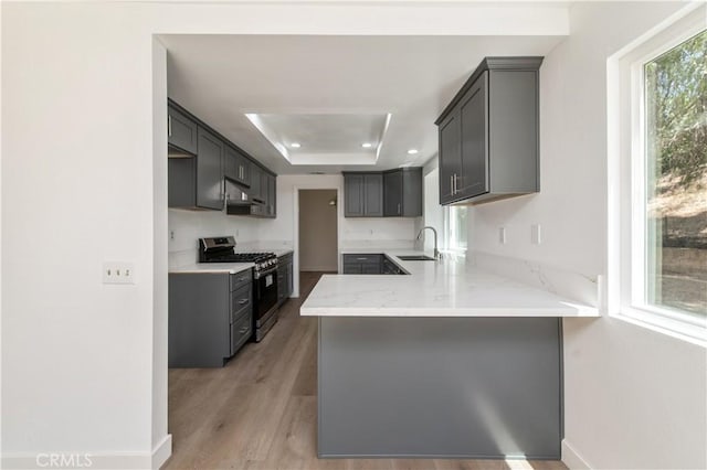 3314 Braemar Ln, Corona, CA 92882 - kitchen with stainless steel gas range, a peninsula, light stone counters, a tray ceiling, and light wood-style flooring
