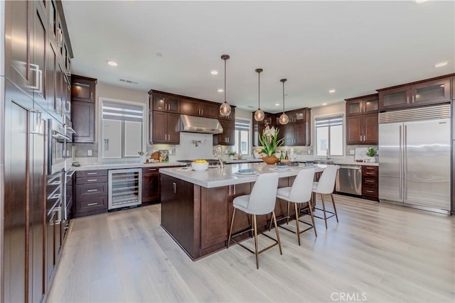 195 Stellar, Irvine, CA 92618 - kitchen with beverage cooler, stainless steel appliances, under cabinet range hood, an island with sink, and light wood finished floors