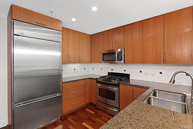 325 7th Ave Unit 609, San Diego, CA 92101 - kitchen with stainless steel appliances, dark stone counters, dark wood-style floors, tasteful backsplash, and brown cabinetry