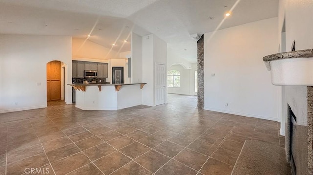 11126 Arena Rd, Pinon Hills, CA 92372 - unfurnished living room with arched walkways, high vaulted ceiling, a fireplace, and dark tile patterned floors