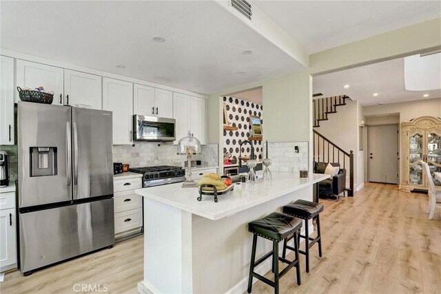 2000 San Antonio Dr, Corona, Corona, CA 92882 - kitchen featuring stainless steel appliances, light wood-style floors, a kitchen breakfast bar, decorative backsplash, and white cabinetry