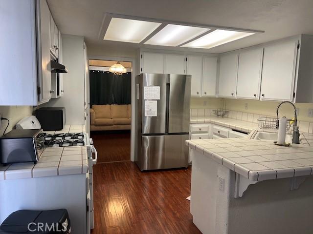 7653 Phelan Rd, Phelan, CA 92371 - kitchen featuring freestanding refrigerator, tile countertops, dark wood-style floors, a peninsula, and under cabinet range hood