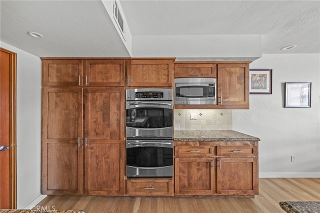4 Woodhaven, Laguna Niguel, CA 92677 - kitchen featuring stainless steel appliances, light wood-style floors, dark stone counters, decorative backsplash, and brown cabinets
