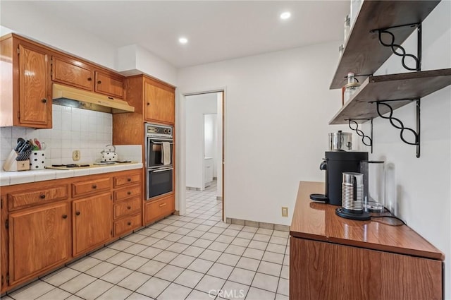 5801 Repetto Ave, East Los Angeles, CA 90022 - kitchen featuring under cabinet range hood, decorative backsplash, white stovetop, light tile patterned flooring, and brown cabinetry