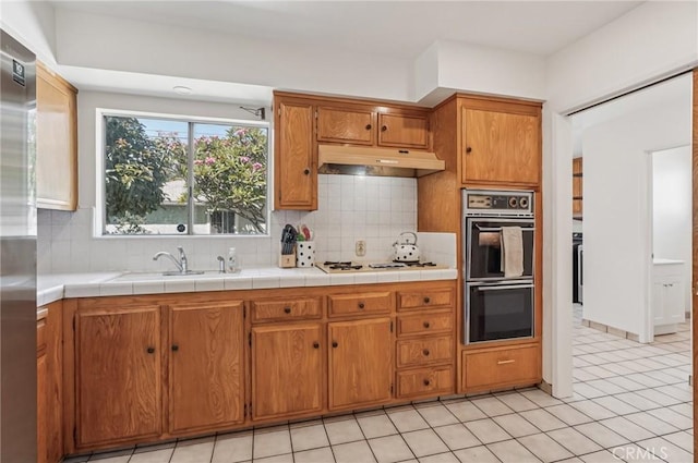 5801 Repetto Ave, East Los Angeles, CA 90022 - kitchen with under cabinet range hood, gas cooktop, brown cabinetry, decorative backsplash, and light tile patterned flooring