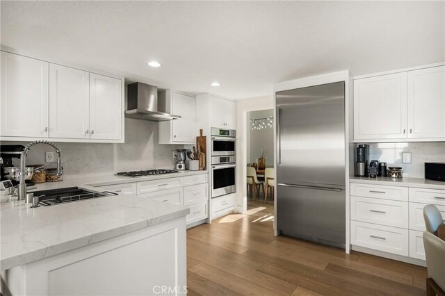 5 Bergamo, Irvine, CA 92614 - kitchen with stainless steel appliances, wall chimney exhaust hood, wood finished floors, white cabinetry, and recessed lighting