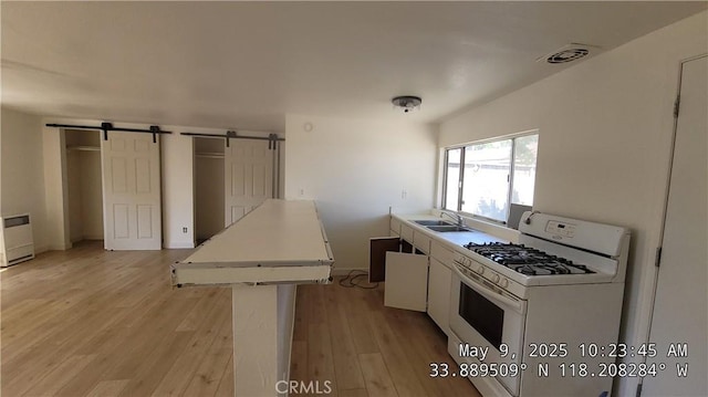 805 S Crane Ave, Compton, CA 90221 - kitchen featuring white range with gas cooktop, a barn door, light wood-type flooring, light countertops, and white cabinetry