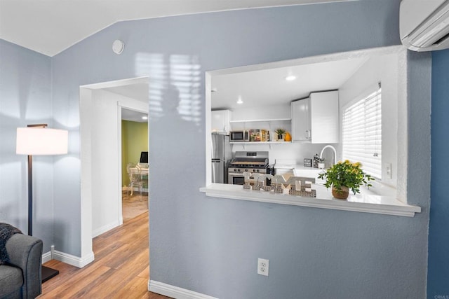 1415 Rex Ln, El Cajon, CA 92021 - kitchen with stainless steel appliances, a wall unit AC, wood finished floors, white cabinetry, and lofted ceiling