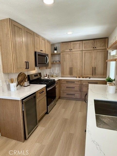 11117 Maidstone Ave, Norwalk, CA 90650 - kitchen featuring stainless steel appliances, open shelves, light wood-type flooring, brown cabinets, and light stone counters