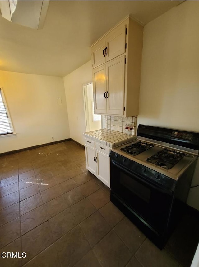 701 Francis St, Bakersfield, CA 93303 - kitchen with black gas range, tile counters, white cabinets, dark tile patterned flooring, and tasteful backsplash