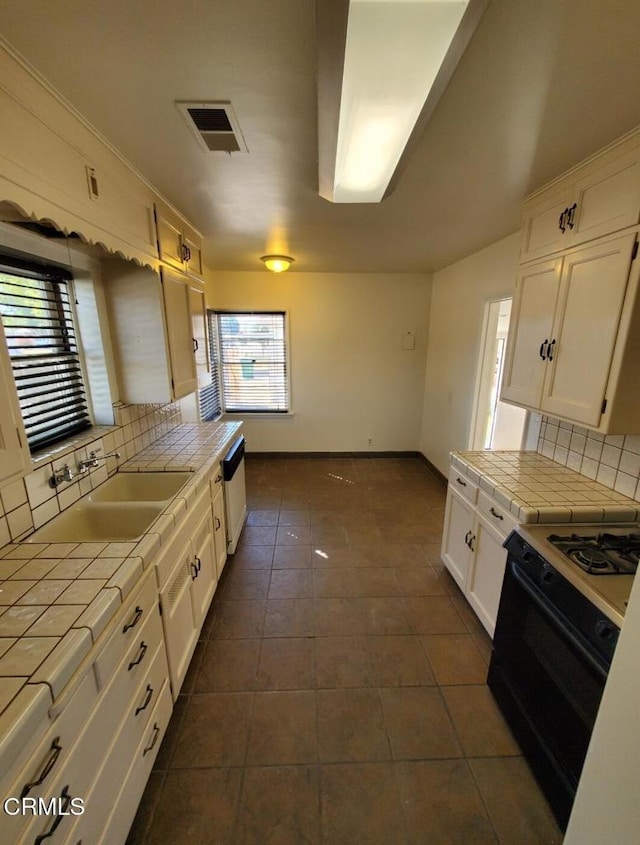 701 Francis St, Bakersfield, CA 93303 - kitchen featuring tile counters, black gas range, backsplash, white cabinetry, and dark tile patterned floors