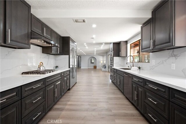 18561 Bert Rd, Riverside, CA 92508 - kitchen with under cabinet range hood, light wood-style floors, stainless steel appliances, backsplash, and recessed lighting