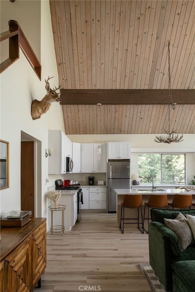 27984 St Bernard Ln, Lake Arrowhead, CA 92352 - kitchen featuring appliances with stainless steel finishes, white cabinetry, open floor plan, a breakfast bar area, and light wood finished floors